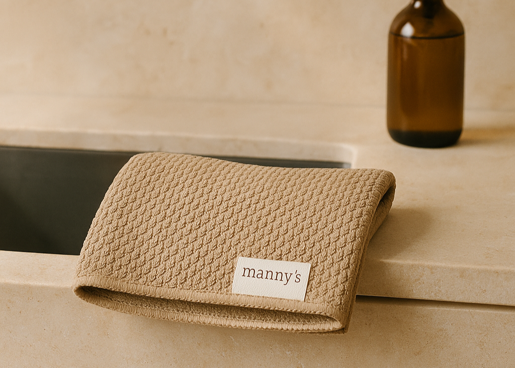 Beige towel with 'manny's' label on a bathroom counter next to a brown bottle.